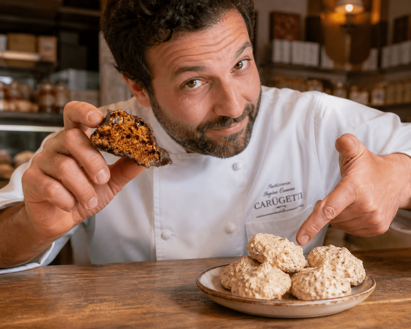 Chef di pasticceria mostra un Carugetto al cioccolato con interno croccante mentre indica dei Brutti e Buoni su un piatto rustico, confronto tra dolci artigianali italiani